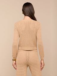 Woman with long brown hair, wearing the Orla Pointelle Knit Cardigan in beige as part of a matching set, facing away from the camera against a plain light background.