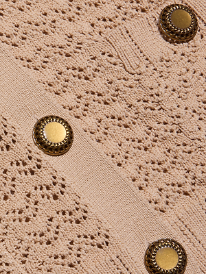 Close-up of the Orla Pointelle Knit Cardigans textured beige fabric with a raised pointelle knit pattern and three decorative gold buttons arranged diagonally—a chic choice for a cover up or lightweight beach sweater.