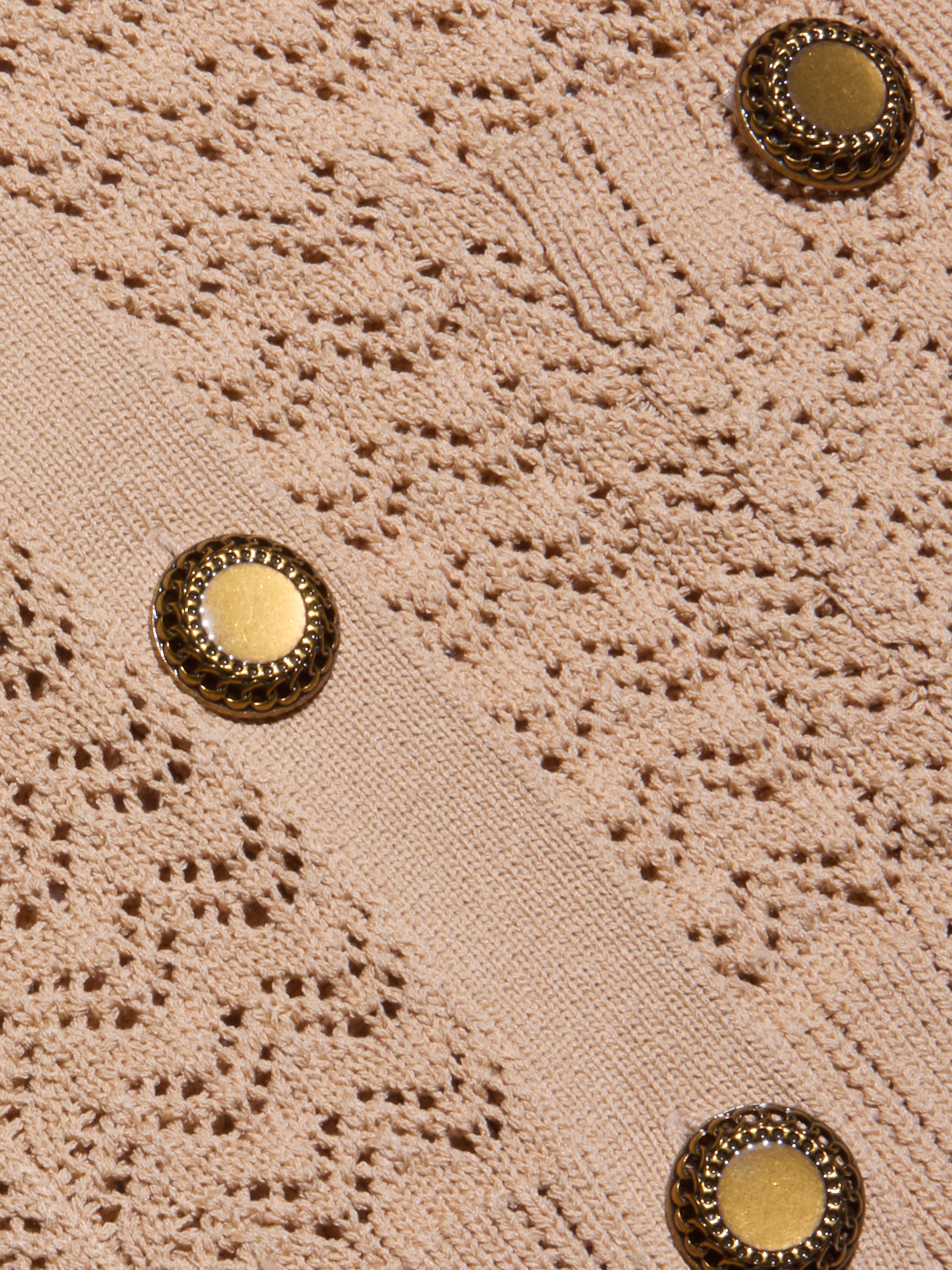 Close-up of the Orla Pointelle Knit Cardigan, featuring textured beige fabric with an intricate lace-like pointelle knit pattern and two round gold buttons with decorative edges.