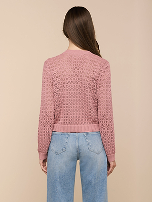 A woman with long brown hair stands facing away, wearing the Orla Pointelle Knit Cardigan in mauve and light blue jeans against a beige background.