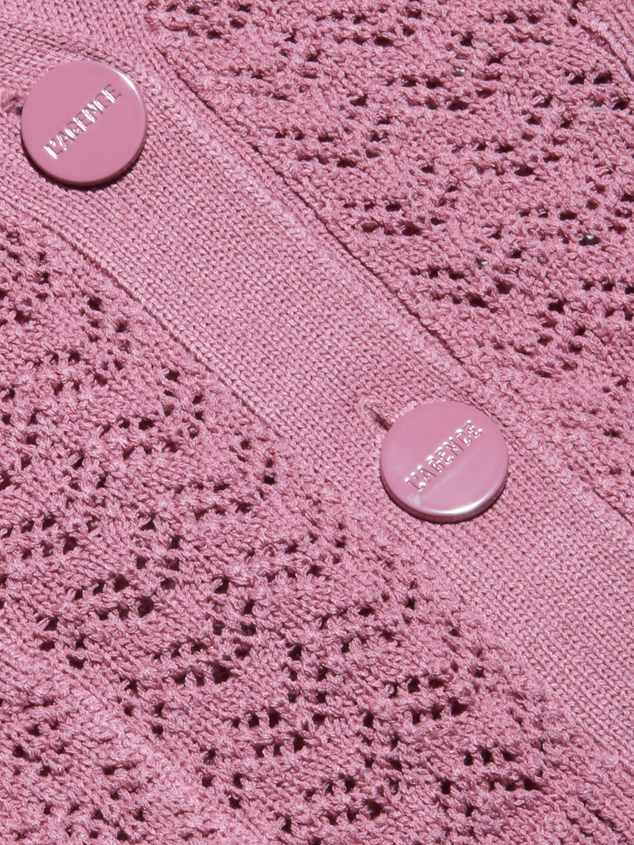 Primo piano del cardigan Orla Pointelle Knit Cardigan color malva, caratterizzato da un motivo a pointelle simile a un merletto e da due bottoni rosa con scritta in rilievo cuciti su una banda verticale solida.