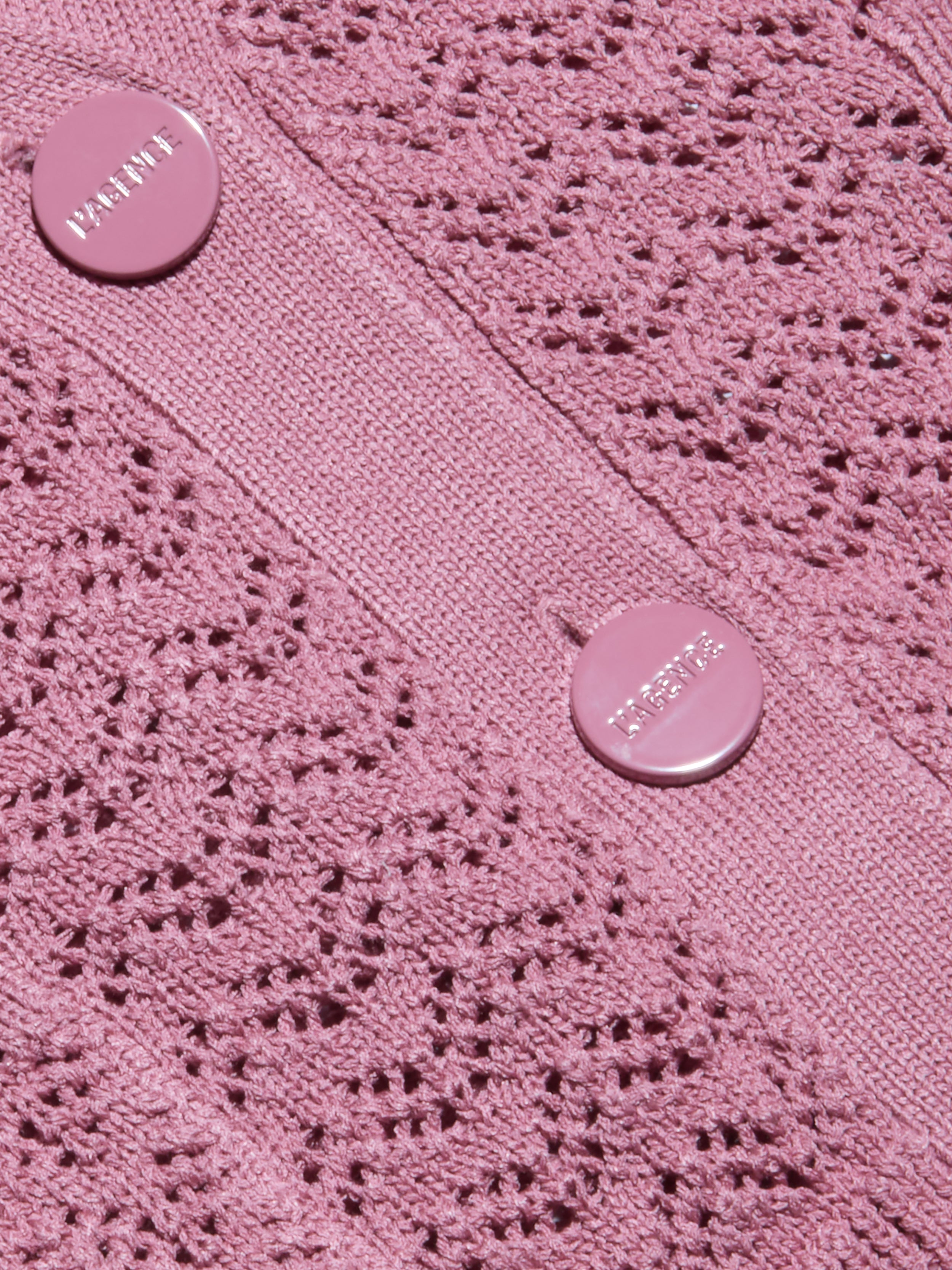 Primo piano del cardigan Orla Pointelle Knit Cardigan color malva, caratterizzato da un motivo a pointelle simile a un merletto e da due bottoni rosa con scritta in rilievo cuciti su una banda verticale solida.