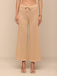 Une femme aux pieds nus présente le pantalon Gaelle Pointelle Knit Pant en beige, avec une texture en crochet, une silhouette à jambes larges et un cordon de serrage à la taille. Elle porte un bracelet en or ; le haut de son corps nest pas visible. Ce pantalon léger est prêt pour les vacances.