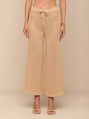 امرأة حافية القدمين تعرض بنطلون Gaelle Pointelle Knit باللون الأسمر، ويتميز بنسيج كروشيه محبوك، وقصة ساق عريضة وخصر برباط. ترتدي سوارًا ذهبيًا؛ الجزء العلوي من جسمها غير ظاهر. هذا البنطلون خفيف الوزن مناسب للعطلات.