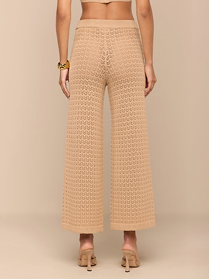 تظهر امرأة من الخلف ترتدي بنطلون Gaelle Pointelle Knit باللون البيج مع صندل بكعب عالٍ وسوار مكتنز، وتقف على خلفية باللون البيج - بنطلون مثالي لقضاء العطلة بأناقة لا تتطلب مجهودًا.