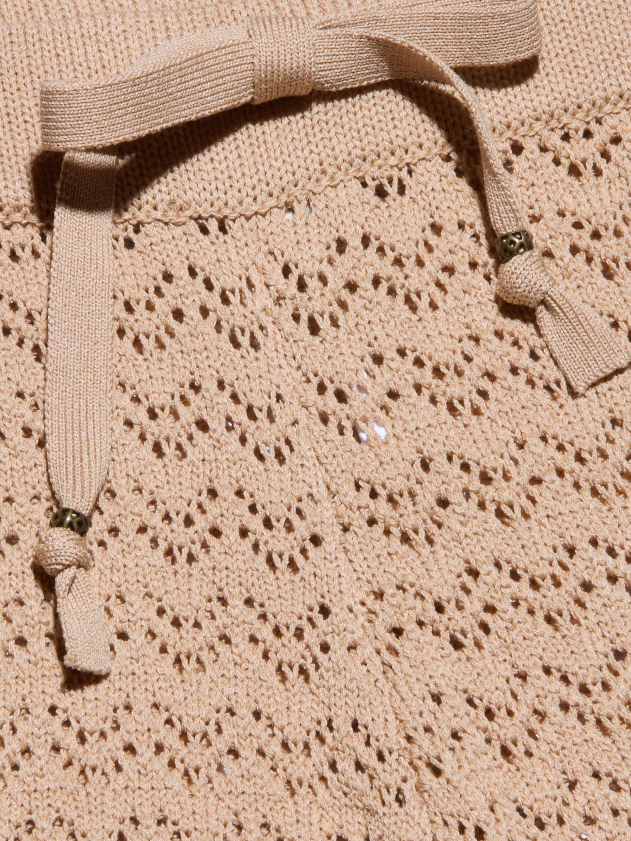 Gros plan sur le pantalon Gaelle Pointelle Knit Pant en beige, montrant son tricot complexe en forme de dentelle et son cordon de serrage assorti avec des accents de perles métalliques - un choix élégant et léger pour les vacances.