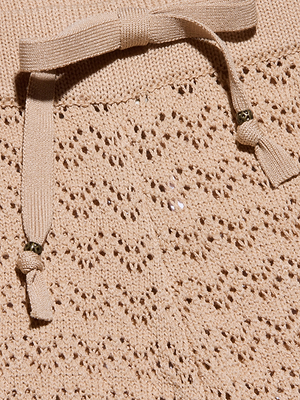 صورة مقرّبة لبنطال Gaelle Pointelle Knit باللون البيج، يظهر فيها الحياكة المعقدة التي تشبه الدانتيل والأربطة المتناسقة مع لمسات من الخرز المعدني - وهو خيار أنيق وخفيف الوزن للارتداء في العطلات.