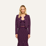 A woman stands facing forward, wearing the Kota Cardigan Top in dark purple with white polka dots and a matching skirt. She has long blonde hair and a neutral expression, with her arms relaxed by her sides against a plain background.
