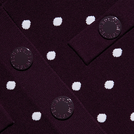 Close-up of the Kota Cardigan Top in dark purple fabric with white polka dots, featuring three round buttons with embossed text sewn onto overlapping fabric panels.