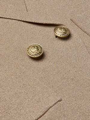 Close-up of the Sofia Knit Blazer by L'AGENCE in beige, featuring textured fabric and two shiny gold embossed crest-and-leaf buttons. The image highlights the elegant details of this double-breasted blazer.