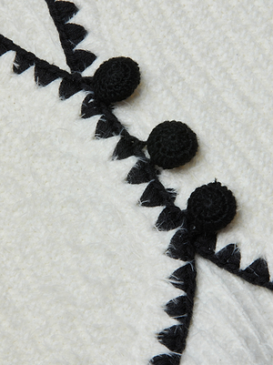 Close-up of the Anaya Knit Cardigan’s textured white fabric, detailed with black embroidered zigzag lines and round black crochet-trim buttons along the stitching.