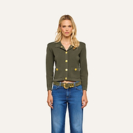 A woman with blonde hair stands facing forward against a plain, light background, wearing the Osiris Cardigan in green crepe knit with gold buttons and blue jeans.