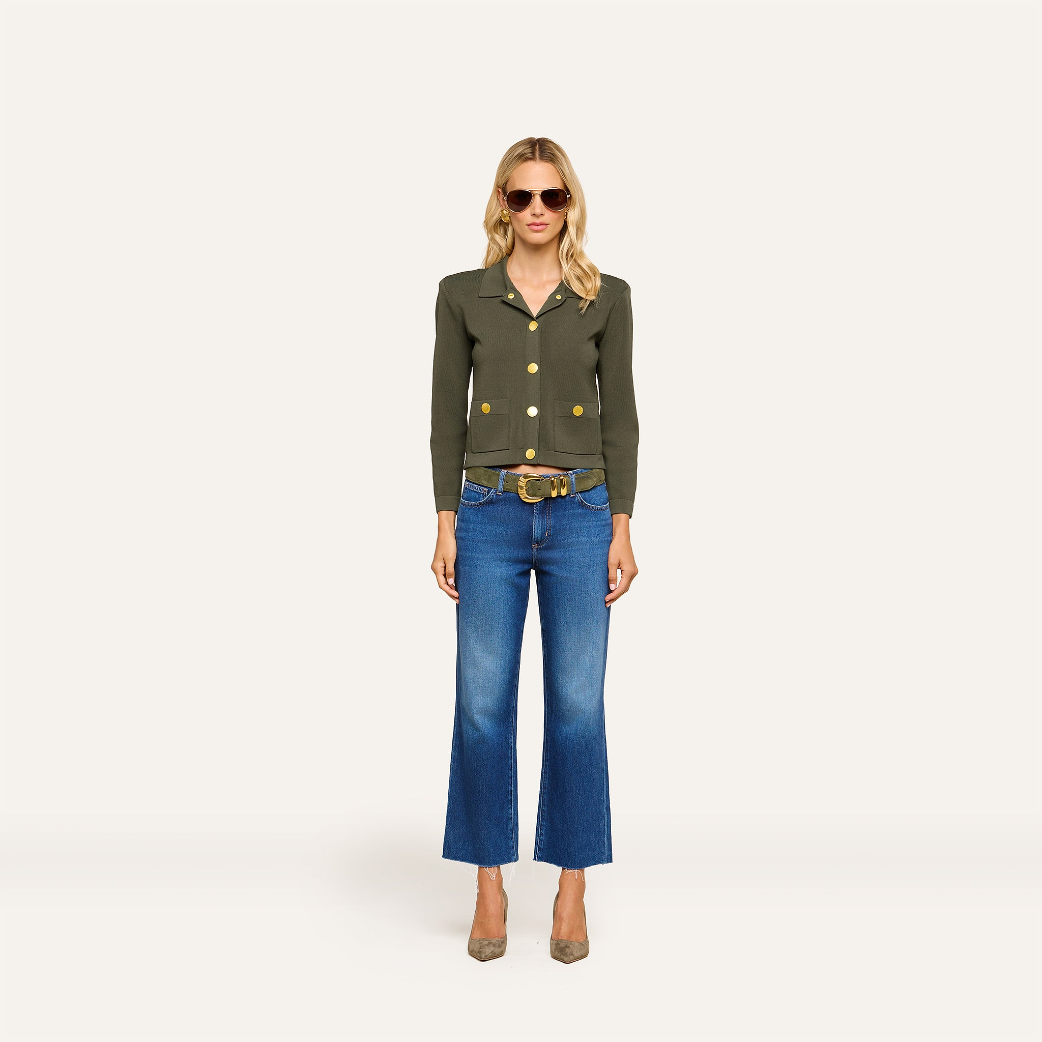 A woman wearing sunglasses, blue jeans, a wide belt, high-heeled shoes, and the Osiris Cardigan stands facing forward against a plain light background.