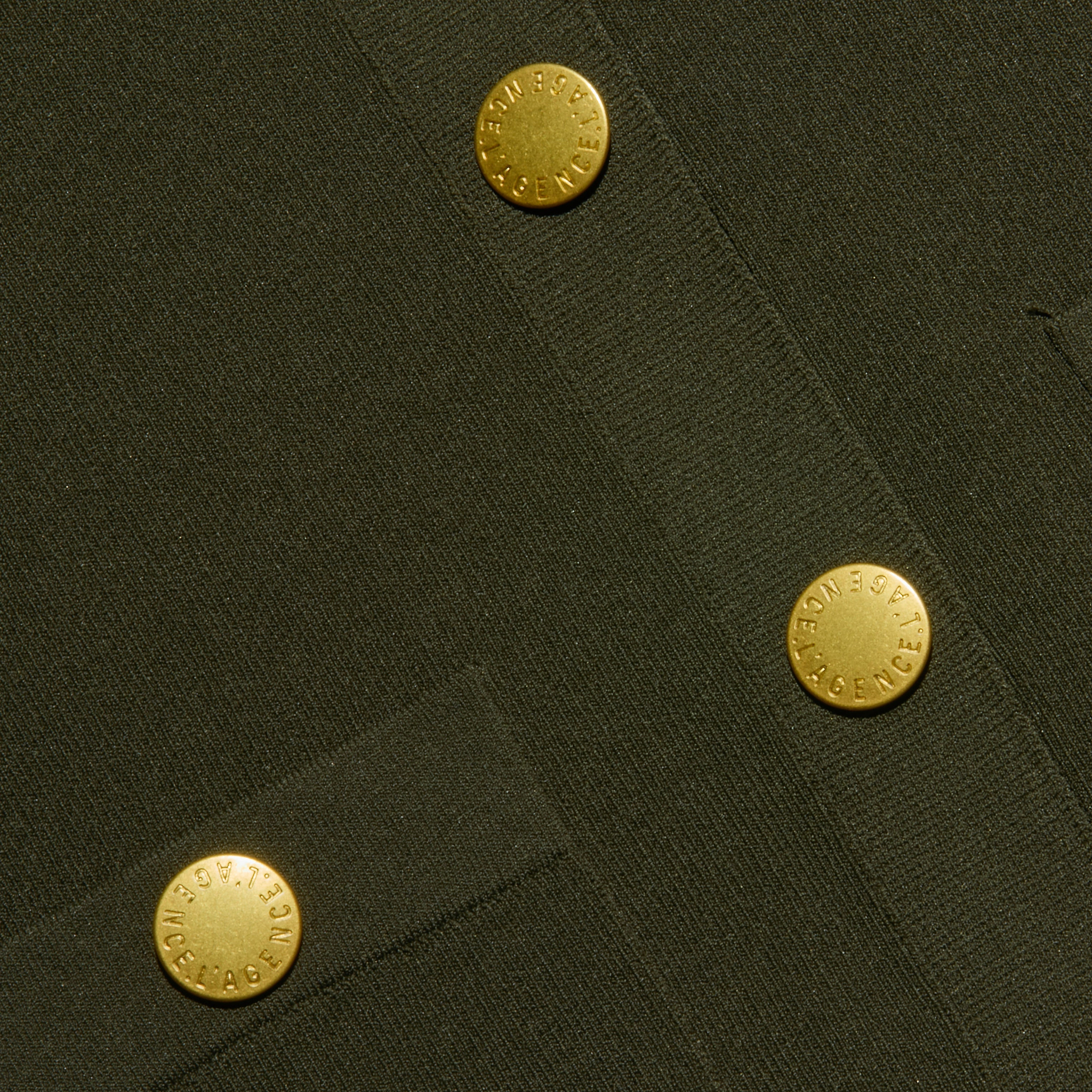 A detailed view of the olive green crepe knit fabric from the Osiris Cardigan highlights three gold buttons engraved with “ABSENCE,” arranged diagonally, while visible pocket seams enhance the textured look.