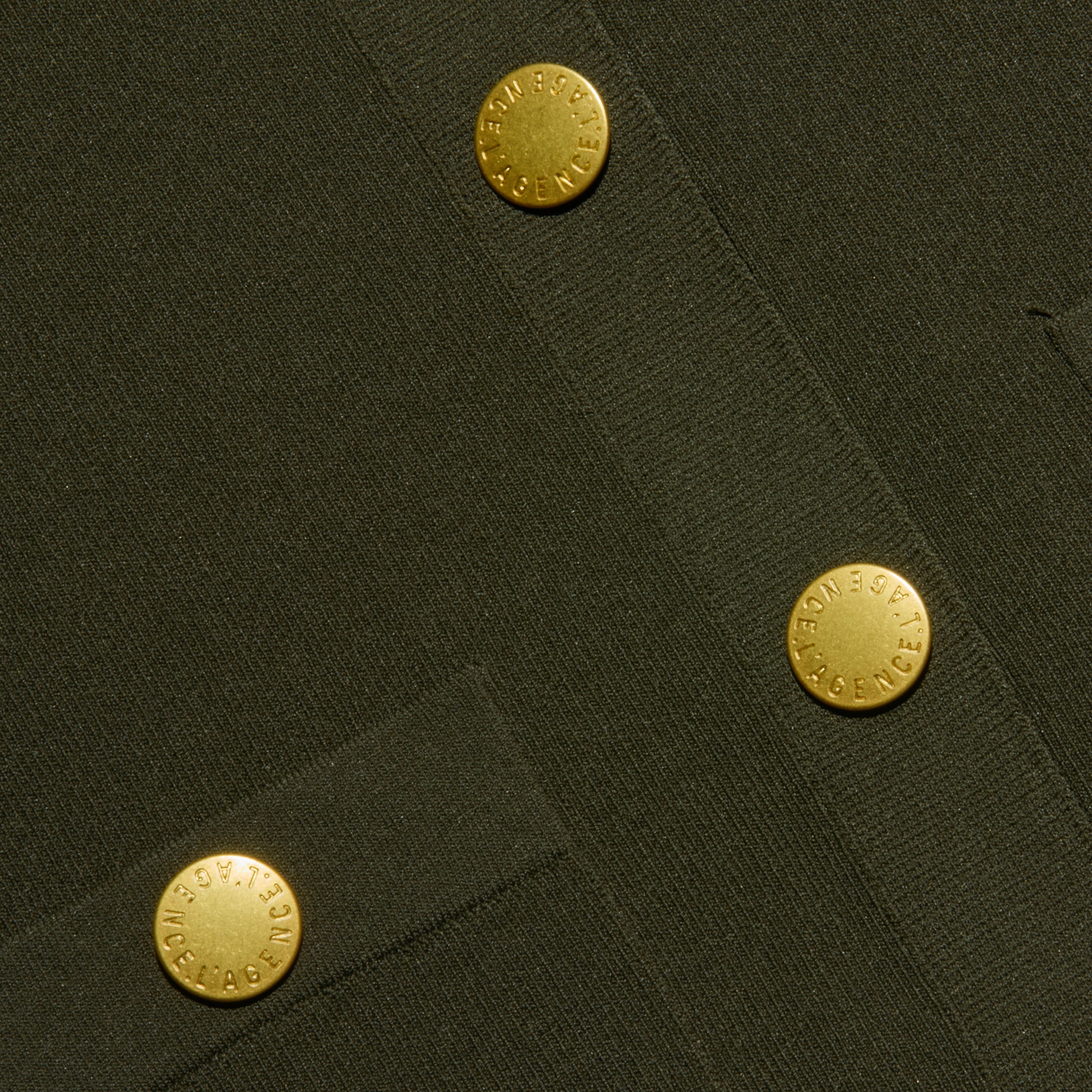 A detailed view of the olive green crepe knit fabric from the Osiris Cardigan highlights three gold buttons engraved with “ABSENCE,” arranged diagonally, while visible pocket seams enhance the textured look.
