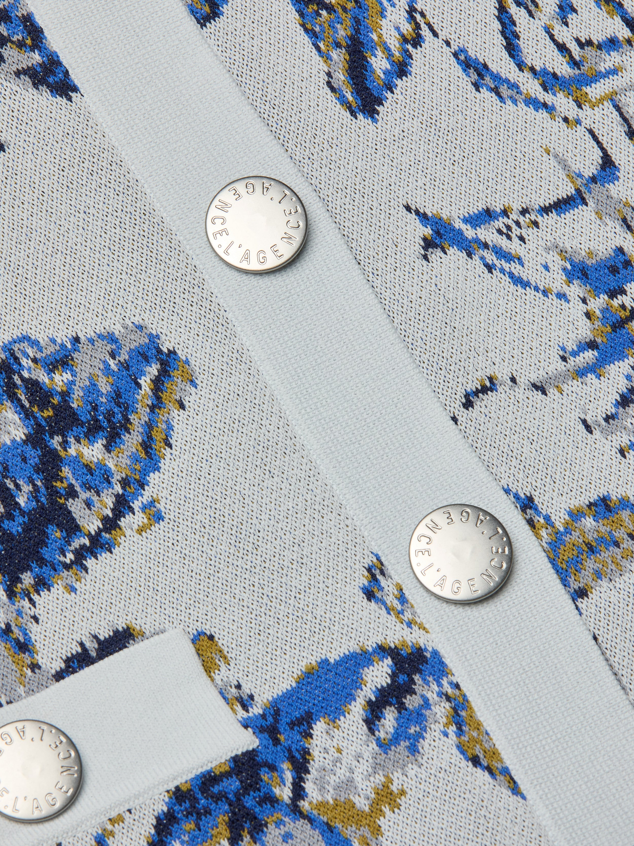 Close-up of the Osiris Jacquard Cardigan in light blue, showcasing its blue, yellow, and white floral jacquard knit with a subtle butterfly motif and finished with silver buttons engraved with text.