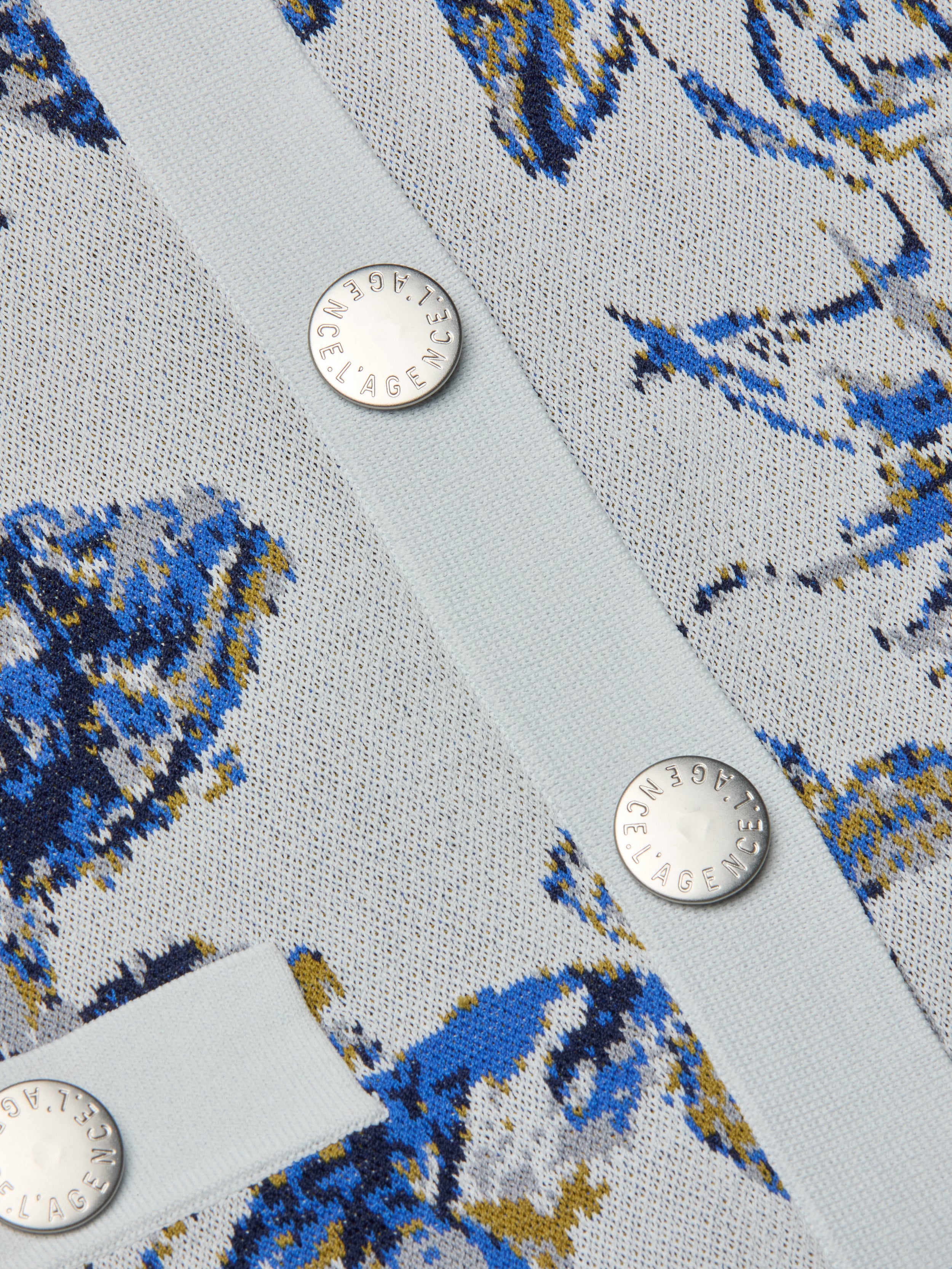 Close-up of the Osiris Jacquard Cardigan in light blue, showcasing its blue, yellow, and white floral jacquard knit with a subtle butterfly motif and finished with silver buttons engraved with text.