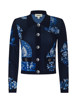 The Osiris Jacquard Cardigan by L'AGENCE features a navy blue jacquard weave with blue porcelain motifs, large silver buttons, a pointed collar, and two front flap pockets with button details.