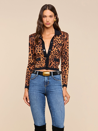 A woman wearing the Osiris Jacquard Cardigan with flap pockets, paired with blue jeans, a black belt featuring a gold buckle, stands against a plain beige background.