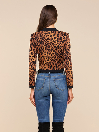A woman stands facing away against a plain beige background, wearing the Osiris Jacquard Cardigan with flap pockets, blue jeans, and black knee-high boots.
