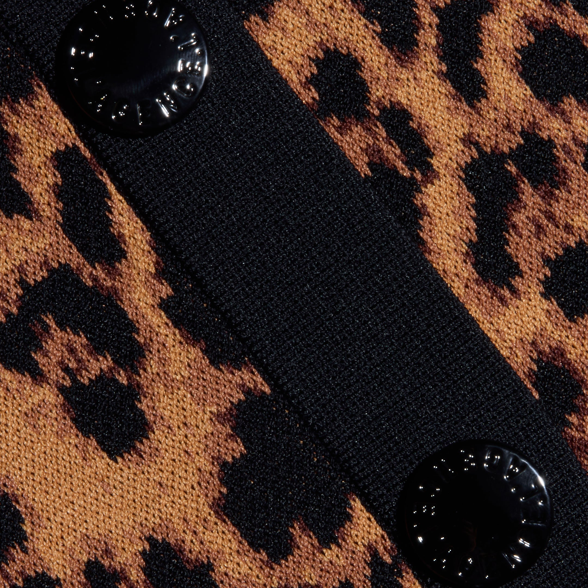 Close-up of the Osiris Jacquard Cardigan, showcasing its leopard print jacquard knit fabric with two black, round buttons sewn onto a black strip that runs diagonally across the patterned material.