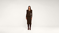A woman stands facing forward in a brown, buttoned jacket and matching skirt with knee-high brown boots, against a plain white background.