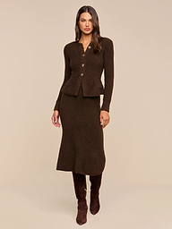 Woman wearing the Melissa Knit Cardigan—a fitted, dark brown blazer crafted from textured knit yarn with button details—paired with a matching midi skirt and knee-high brown boots, standing against a plain beige background for an elegant take on women’s knitwear.