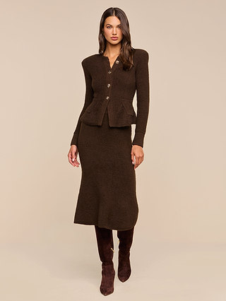 Woman wearing the Melissa Knit Cardigan—a fitted, dark brown blazer crafted from textured knit yarn with button details—paired with a matching midi skirt and knee-high brown boots, standing against a plain beige background for an elegant take on women’s knitwear.