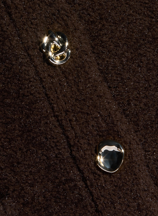 Close-up of a dark brown textured yarn fabric with two shiny, gold-toned buttons. The fabric appears thick, possibly wool or fleece, and the buttons have unique, irregular shapes—perfect for a stylish piece of women’s knitwear like the Melissa Knit Cardigan.