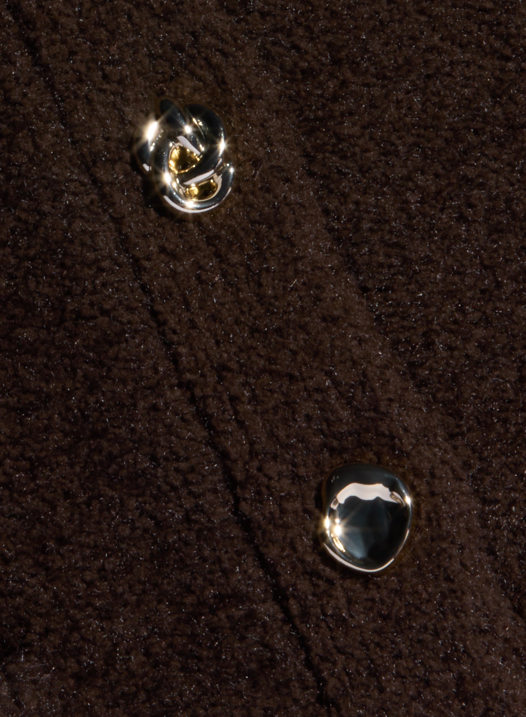 Close-up of a dark brown textured yarn fabric with two shiny, gold-toned buttons. The fabric appears thick, possibly wool or fleece, and the buttons have unique, irregular shapes—perfect for a stylish piece of women’s knitwear like the Melissa Knit Cardigan.
