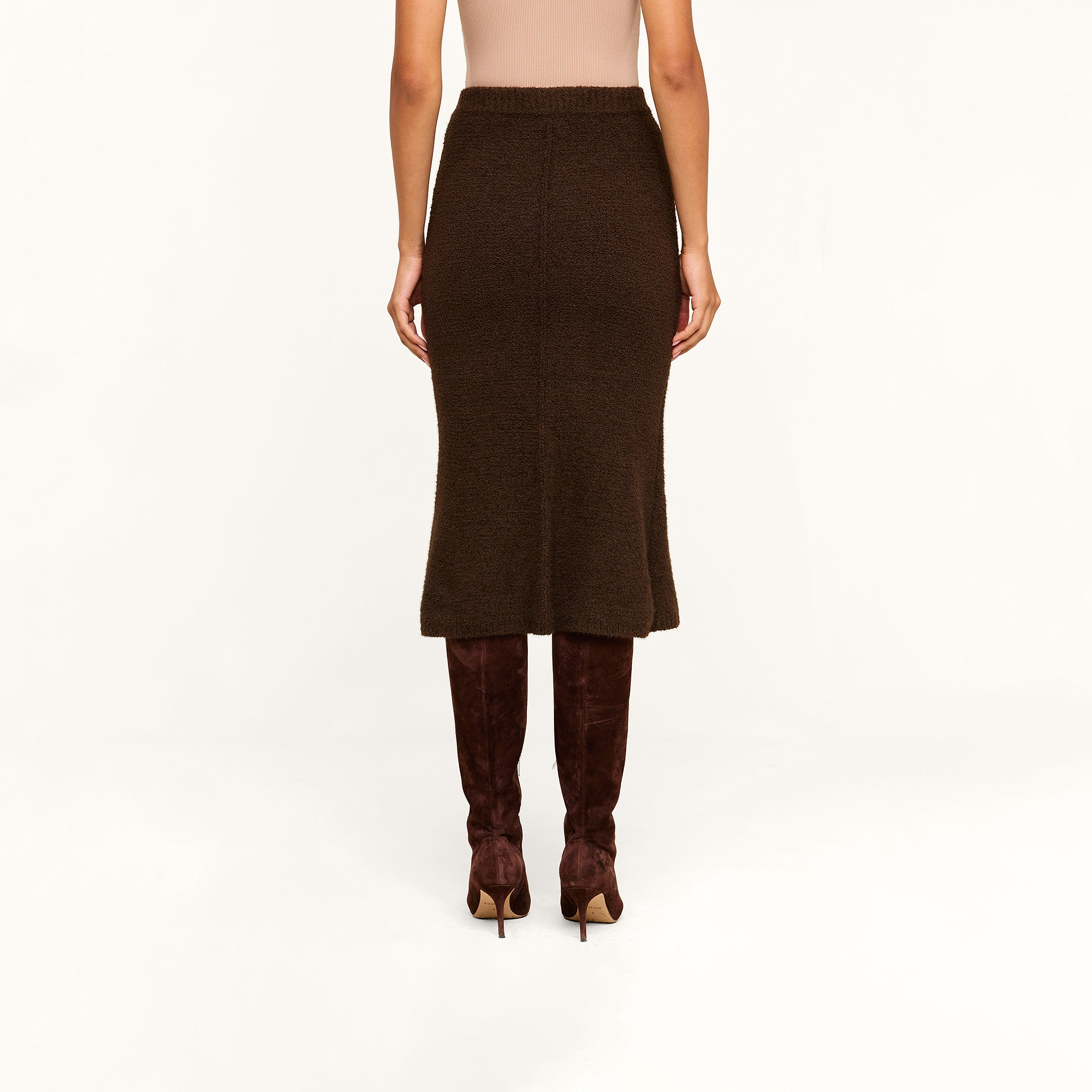 A person wearing the Salem Knit Skirt in brown, paired with brown suede knee-high boots, is standing against a beige background. The image captures the back view from shoulders to feet.