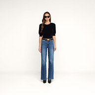 A woman wearing sunglasses, the Guinevere Cropped Pullover—an ultra soft knit black top with a cropped silhouette—blue high-waisted jeans, and black boots stands facing forward against a plain white background.