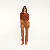 A woman wearing sunglasses and the Guinevere Cropped Pullover—a rust-colored ultra soft knit short-sleeve top with a cropped silhouette—paired with tan leather pants, a tan belt, and tan shoes stands against a plain white background.