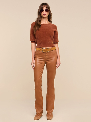 A woman wearing sunglasses, the ultra-soft Guinevere Cropped Pullover in rust with a crewneck and cropped silhouette, tan leather pants with a belt, and tan shoes stands against a beige background.