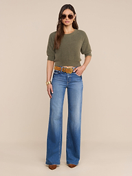 A woman wearing sunglasses, the Guinevere Cropped Pullover in olive green, wide-leg blue jeans with a belt, brown pointed-toe shoes, and a gold bracelet stands against a plain white background.