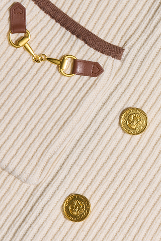 Close-up of the Ranch Knit Blazer, showcasing cream-colored ribbed knit fabric with brown trim, a decorative leather and gold buckle detail, and two gold lion head buttons inspired by classic double-breasted blazer design.