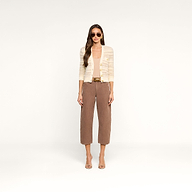 Wearing the Ariadne Cardigan, a woman with long wavy hair stands against a white background. She wears sunglasses, a white top, brown cropped pants with a belt, and open-toe heels, showcasing a neutral expression.