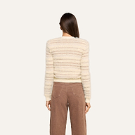A person with straight brown hair, seen from behind, wears the Ariadne Cardigan—a cream and beige striped cotton-blend sweater—paired with high-waisted brown corduroy pants against a plain light background.