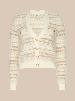 The Ariadne Cardigan, showcased on a beige background, features cream and pink stripes in mixed stitches and eyelash yarns, crafted from a cotton-blend. It is finished with gold ring buttons and grommet accents.