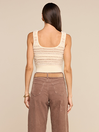 A woman with long brown hair, wearing the Galene Tank—a sleeveless cream knit top with vintage-style buttons—and high-waisted brown corduroy pants, stands with her back to the camera against a beige background.