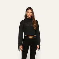 A woman wears a marled black Maddison Turtleneck featuring a cropped fit, fringe detailing on the sleeves, and a black belt with a gold buckle.