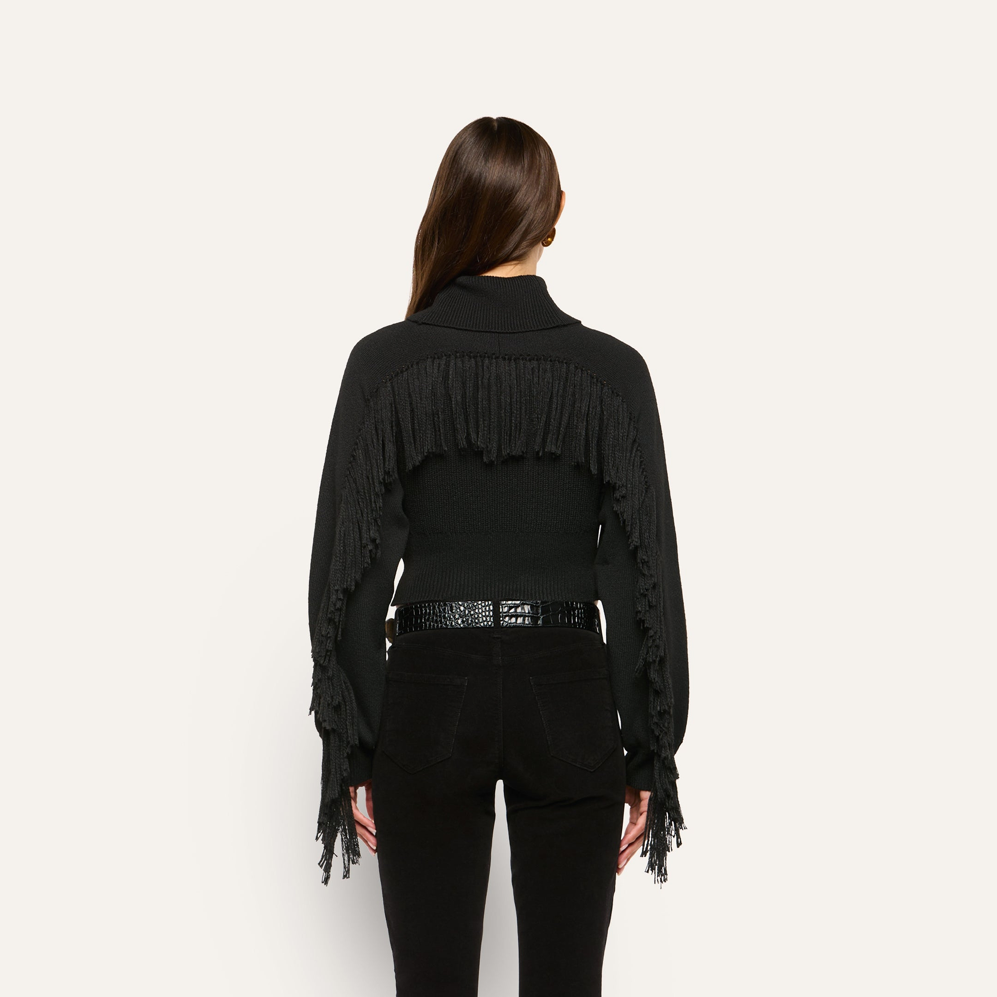 Back view of the black Maddison Turtleneck, a cropped sweater featuring fringe detail across the shoulders and down the sleeves.