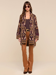Woman wearing sunglasses, a boho-chic patterned brown Jair Cardigan, brown top, and brown flared pants stands against a plain white background.