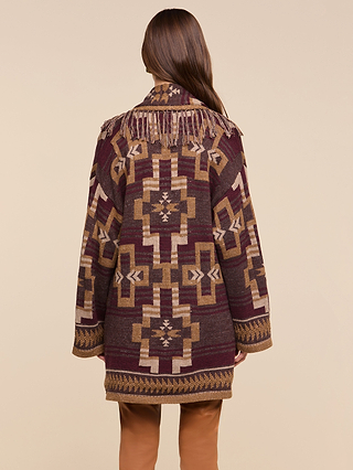A person with long brown hair wears the Jair Cardigan—a boho-chic, patterned maroon, brown, and beige coat featuring fringe on the shoulders—standing with their back to the camera against a beige background.