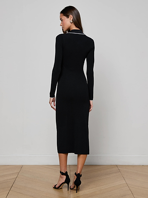 A woman faces away, wearing the Yaretzi Knit Midi Dress by L'AGENCE Sale with long sleeves and black heels. She stands on a light wooden floor against a plain white wall.
