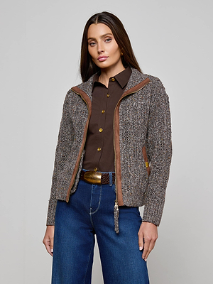 A woman with long brown hair models the L'AGENCE Shiloh Cable Knit Cardigan, styled with blue jeans and a wide belt, standing against a plain light background.