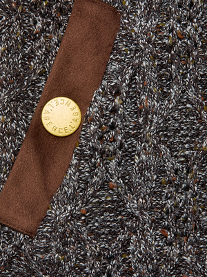 A close-up of the Shiloh Cable Knit Cardigan by L'AGENCE, featuring textured gray cable knit, a brown vegan suede trim, and a round gold button engraved with 