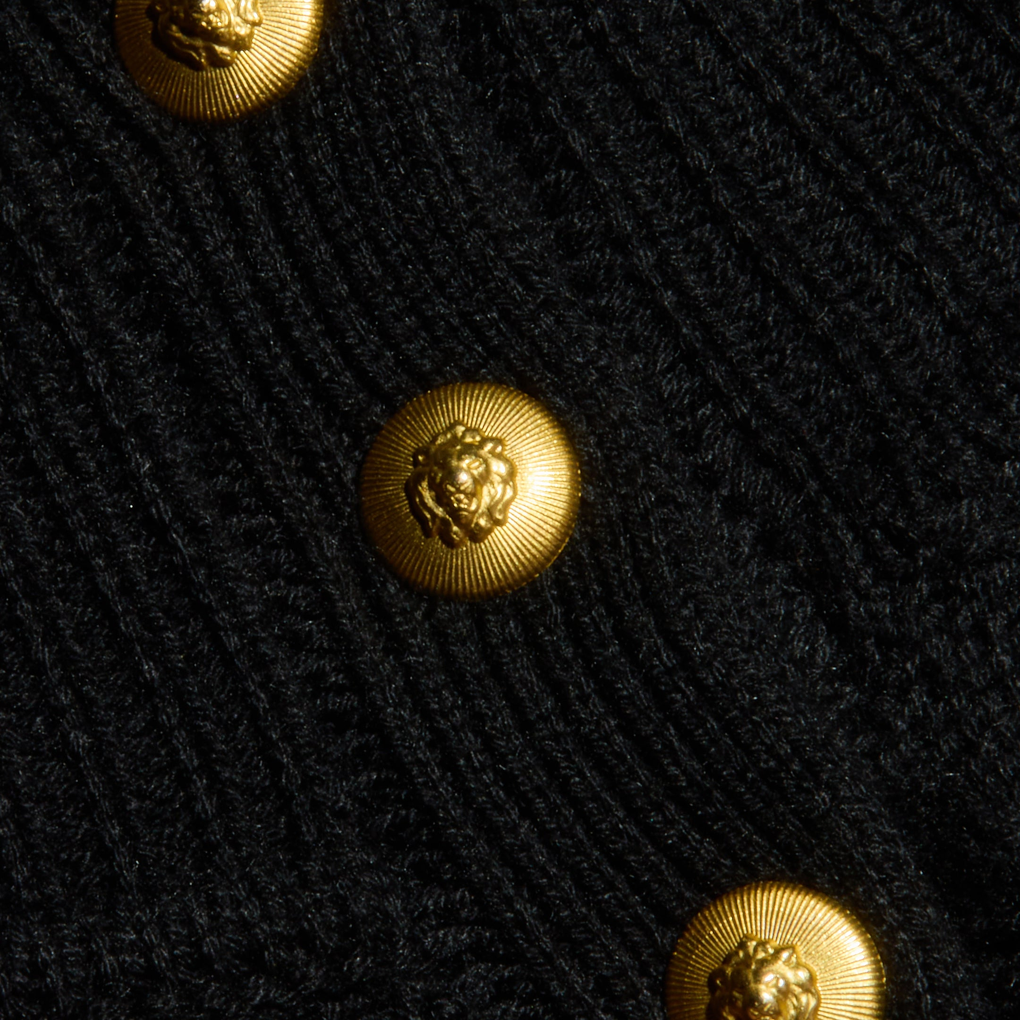 Close-up of the Kamdyn Cropped Sweater—a black ribbed mockneck style adorned with shiny gold buttons, each embossed with a lion’s head in relief.
