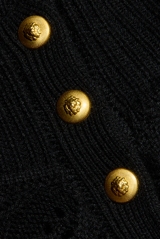 Close-up of the Kamdyn Cropped Sweater in black, featuring a cable knit texture and a mockneck with three vertically arranged gold buttons, each adorned with an embossed lion’s head design.