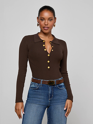 A woman wears the Elisabetta Knit Bodysuit—a brown long sleeve polo with gold buttons—paired with blue jeans and a brown belt. She accessorizes with hoop earrings, her hair pulled back, standing against a light gray background.